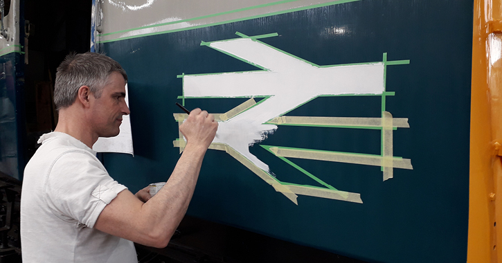 A volunteer at Locomotion helps paint the exterior of a train